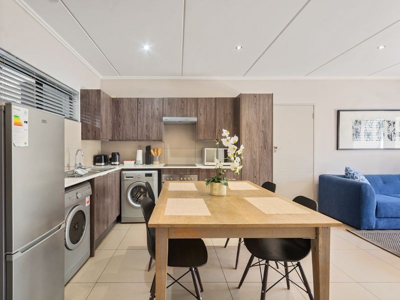 Modern open-plan kitchen and dining area featuring wood-grain cabinetry, integrated appliances, tiled flooring, and recessed lighting, seamlessly flowing into the living space.