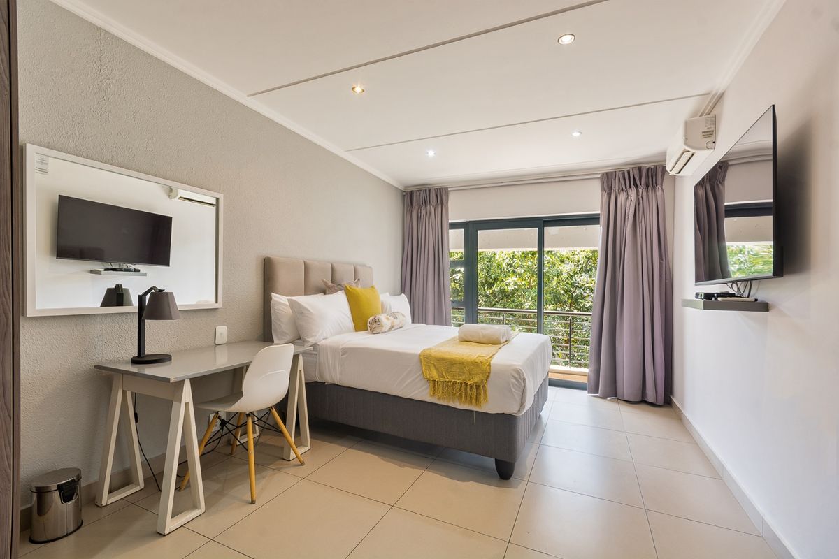 A well-maintained bedroom featuring tiled flooring, recessed lighting, a wall-mounted air conditioning unit, and a sliding glass door leading to a balcony.