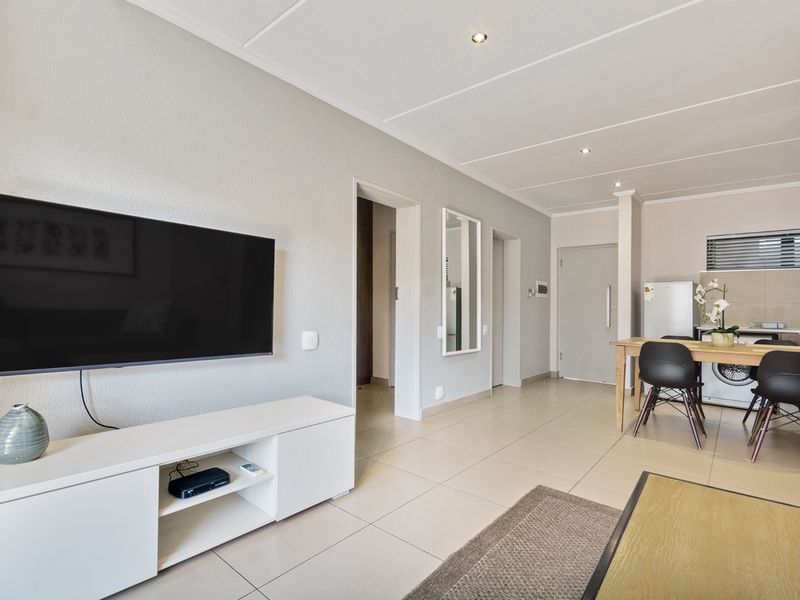 An open-plan living and kitchen area featuring neutral tiled flooring, recessed ceiling lights, and a functional kitchen layout with built-in cabinetry.