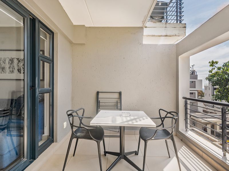 A covered balcony featuring tiled flooring, a metal balustrade, and access via a sliding glass door, offering an outdoor space for relaxation.