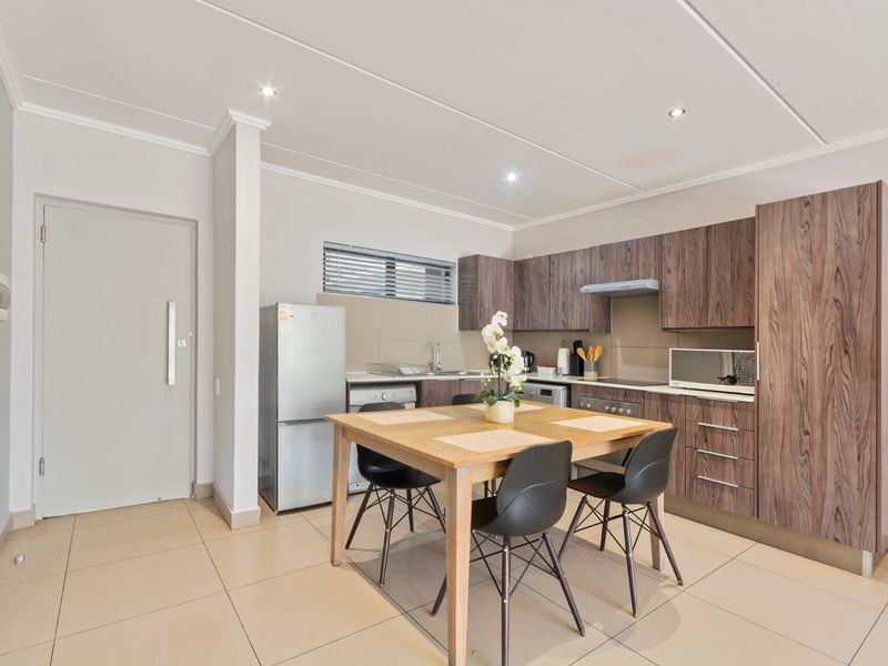 Modern open-plan kitchen and dining area featuring wood-grain cabinetry, tiled flooring, and recessed lighting, creating a functional and cohesive living space.