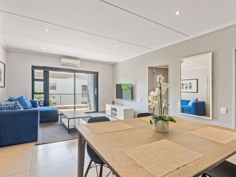 A bright open-plan living and dining area featuring tiled floors, recessed lighting, air conditioning, and direct access to a private balcony.