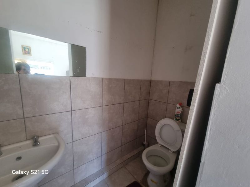 A compact bathroom featuring a wall-mounted basin, toilet, and partial wall tiling, currently showing signs of wear and wall surface damage.