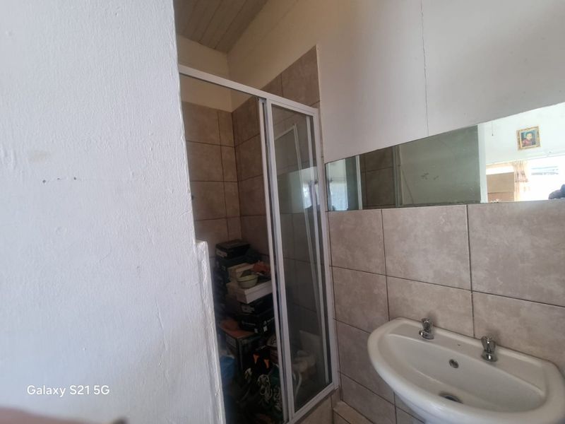 A functional bathroom featuring a shower enclosure, wall-mounted basin, and tiled splashback, currently used for storage.
