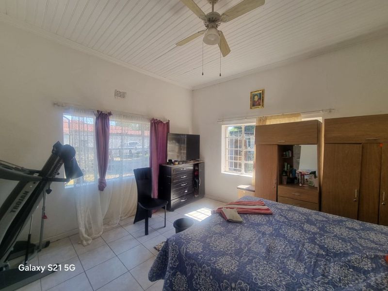 A bedroom featuring tiled flooring, a ceiling fan, and timber-look ceiling panels, providing a functional space with natural light through multiple windows.