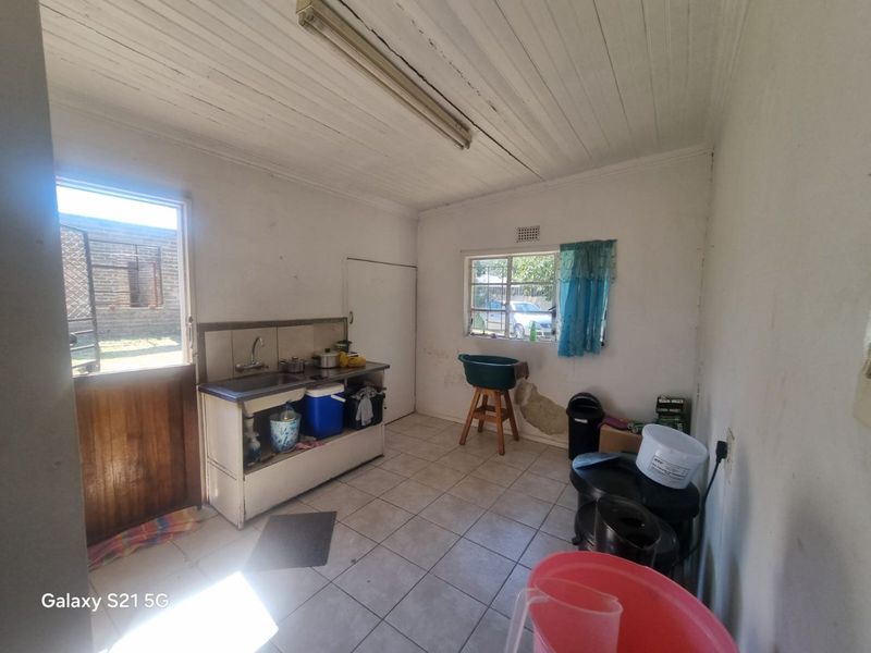 A functional laundry area featuring tiled flooring, a single basin sink, and direct access to the exterior, requiring cosmetic updates and wall repairs.