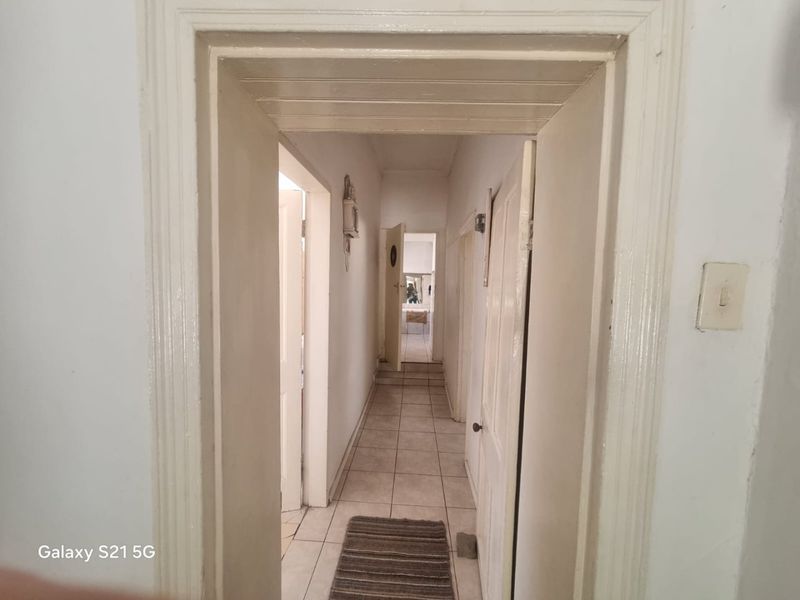 A narrow interior hallway featuring tiled flooring and multiple doorways leading to adjacent rooms, showing signs of wear and dated finishes.