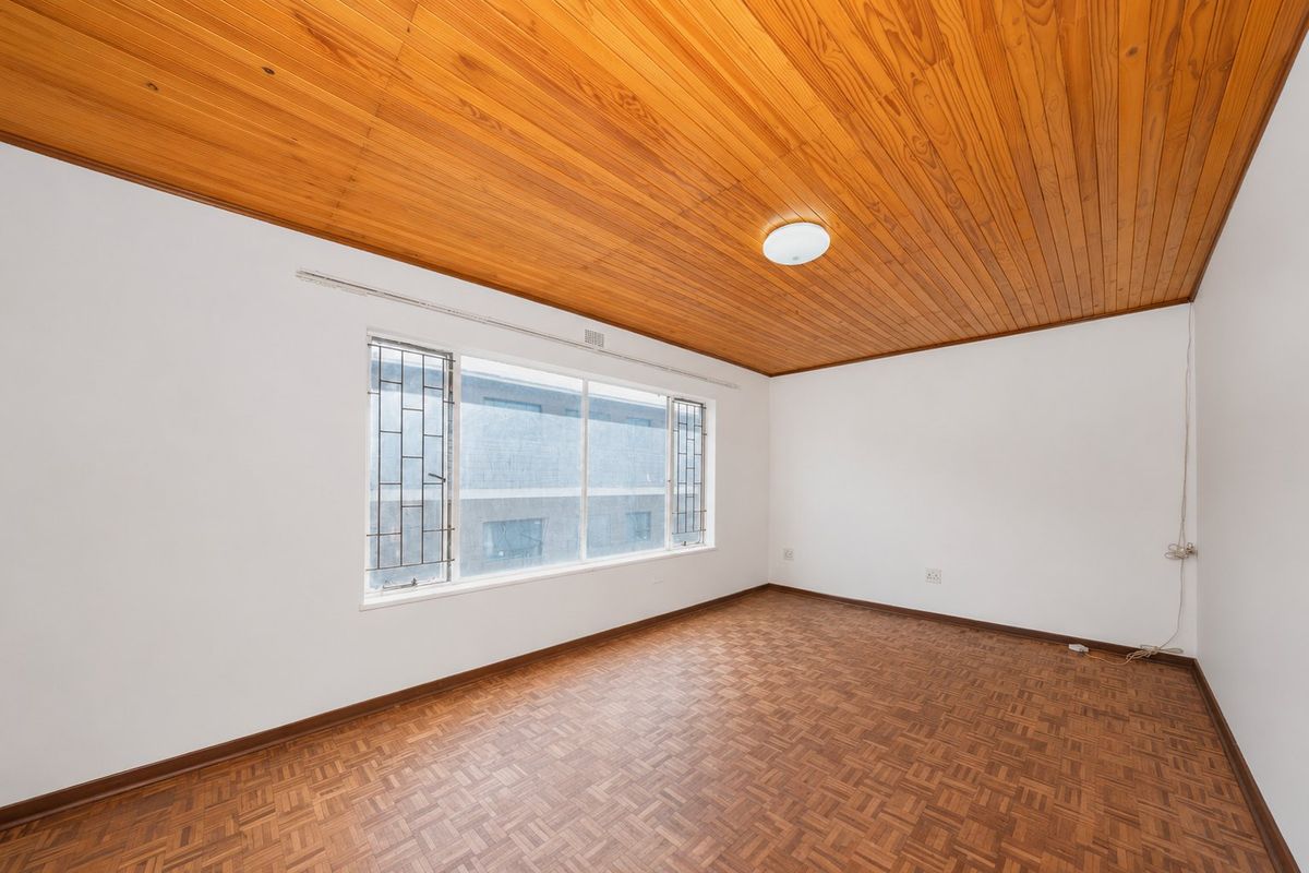 An empty bedroom featuring parquet flooring, a timber-clad ceiling, and a large window fitted with security bars.