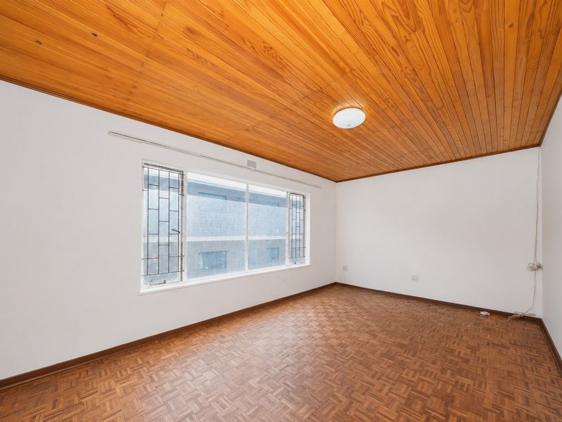 An empty bedroom featuring parquet flooring, a timber-clad ceiling, and a large window fitted with security bars.