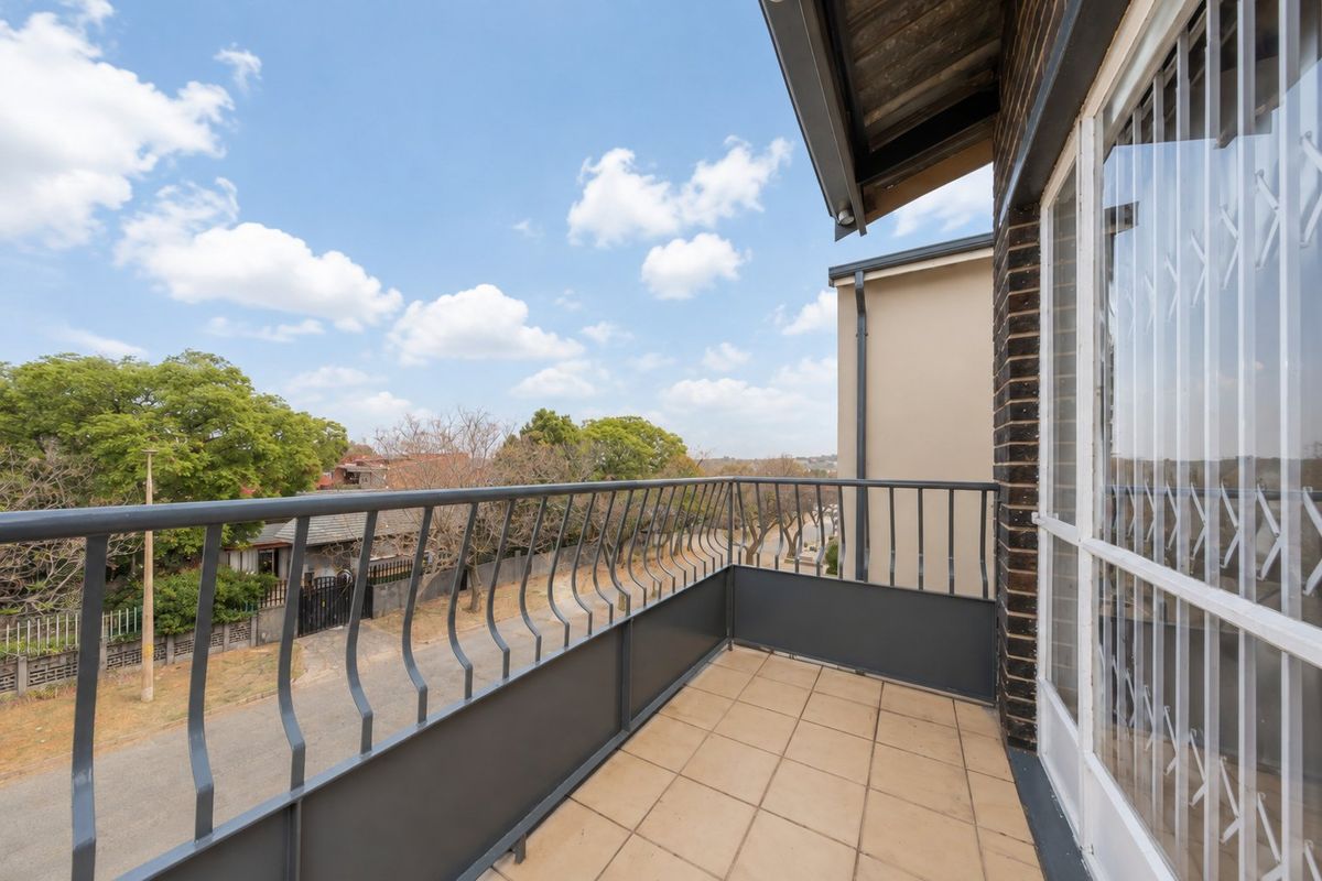 A clean, open-air balcony featuring tiled flooring and a secure metal balustrade, offering clear views of the surrounding neighborhood.