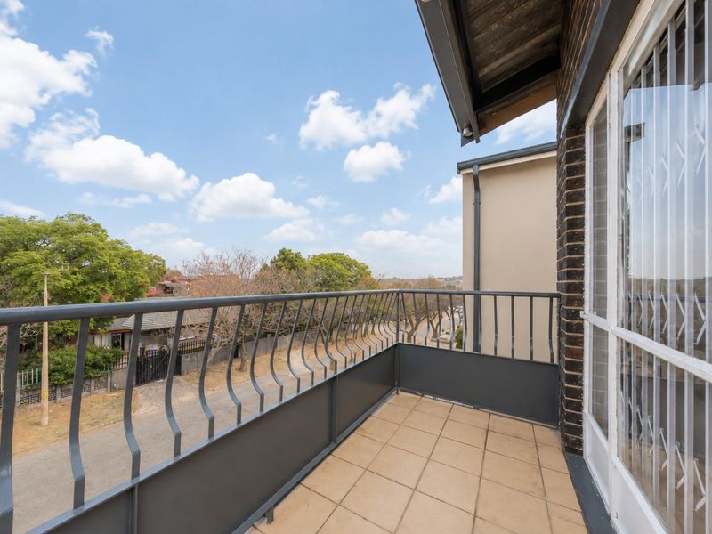 A clean, open-air balcony featuring tiled flooring and a secure metal balustrade, offering clear views of the surrounding neighborhood.