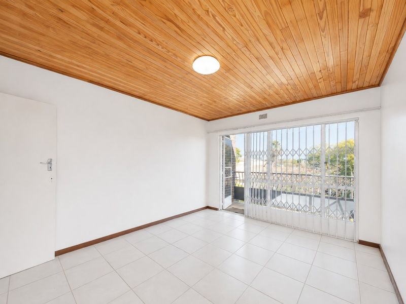 An empty living room featuring a timber-clad ceiling, tiled flooring, and a sliding glass door with a security gate leading to a balcony.