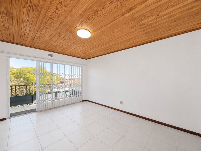 An empty living room featuring ceramic floor tiles, a distinctive wooden tongue and groove ceiling, and a sliding glass door leading to a balcony.