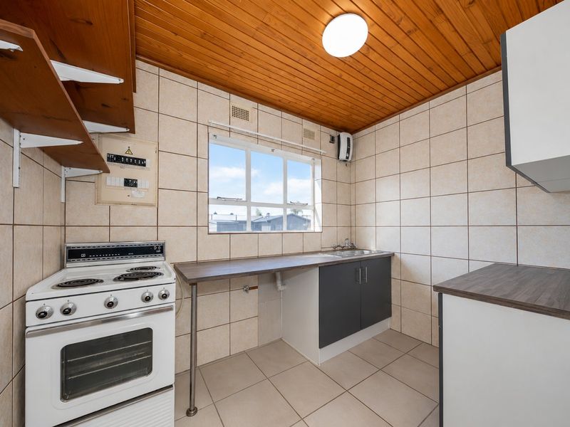 A functional kitchen featuring tiled walls, laminate countertops, a freestanding stove, and a timber-clad ceiling, offering a clean space ready for modernization.
