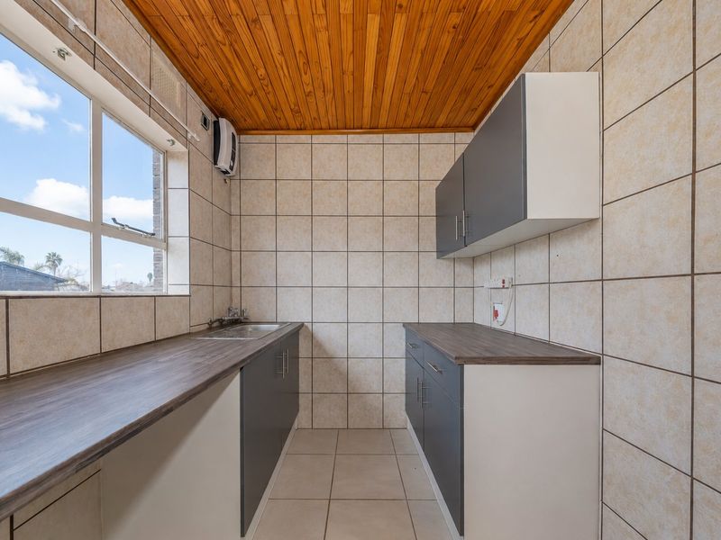 A functional scullery featuring laminate countertops, built-in cabinetry, a stainless steel sink, and tiled finishes with a timber ceiling.
