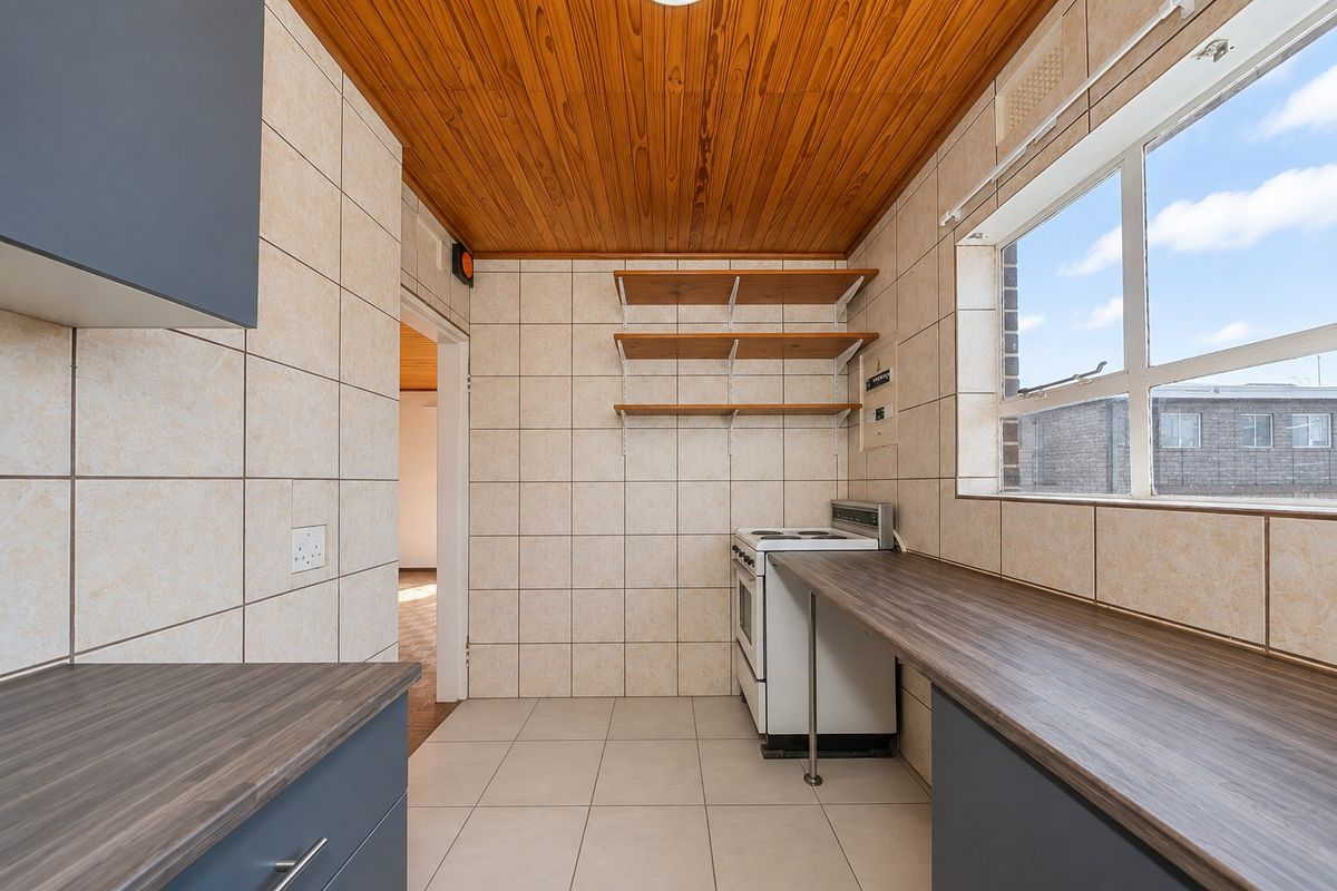 A functional kitchen featuring tiled walls, laminate countertops, a freestanding stove, and a distinctive wooden ceiling, offering a clean and practical workspace.