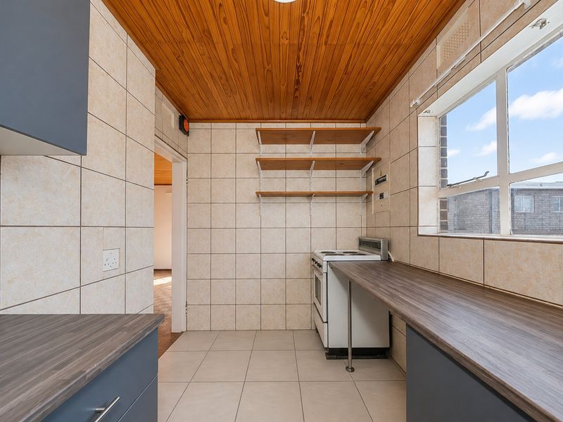A functional kitchen featuring tiled walls, laminate countertops, a freestanding stove, and a distinctive wooden ceiling, offering a clean and practical workspace.