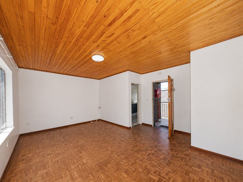 An empty living room featuring classic parquet flooring and a warm wooden ceiling, with direct access to an exterior balcony area.