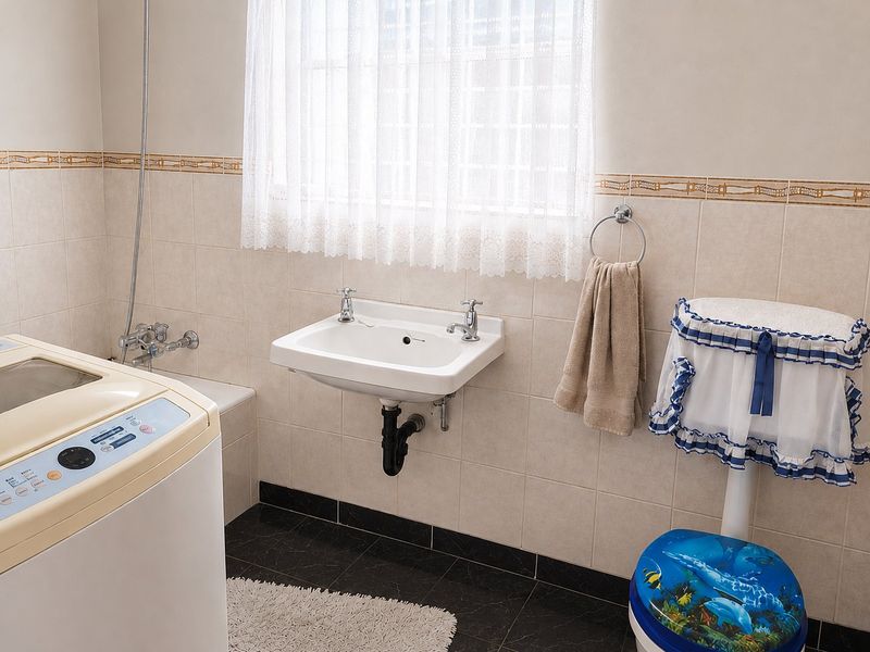 A functional bathroom featuring a wall-mounted basin, toilet, and tiled finishes, offering a clean and practical space with potential for modern updates.