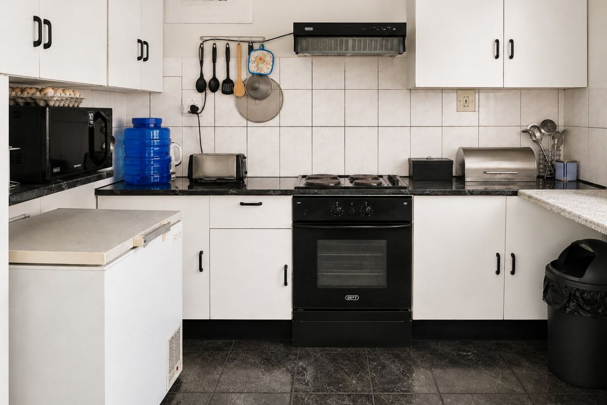 A functional kitchen featuring white cabinetry, dark countertops, tiled backsplash, and a built-in electric oven with extractor fan.