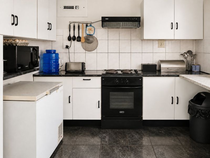A functional kitchen featuring white cabinetry, dark countertops, tiled backsplash, and a built-in electric oven with extractor fan.