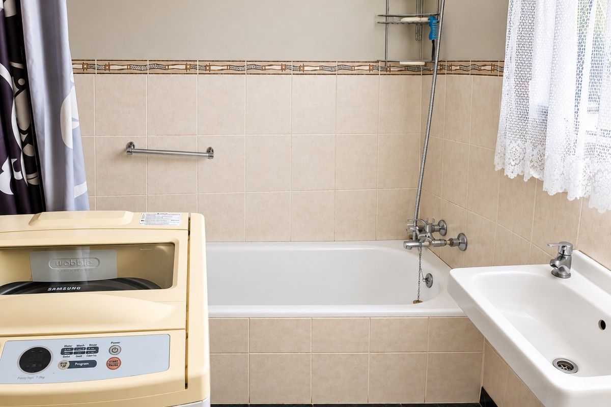 A functional bathroom featuring a bathtub with shower mixer, wall-mounted basin, and neutral wall tiling.