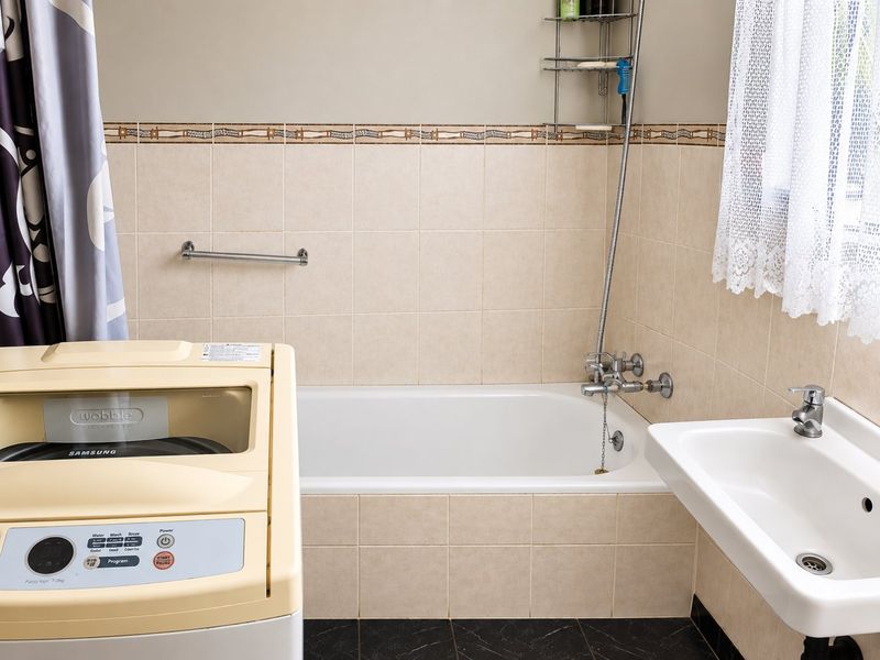 A functional bathroom featuring a bathtub with shower mixer, wall-mounted basin, and neutral wall tiling.