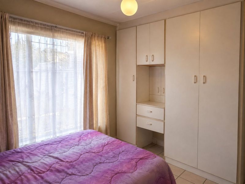 A bedroom featuring built-in cupboards with integrated vanity storage, tiled flooring, and a large window with security gate access.