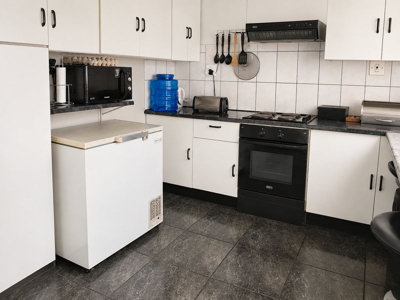 Functional kitchen featuring white cabinetry, dark laminate countertops, tiled backsplash, and built-in electric oven with hob and extractor fan.