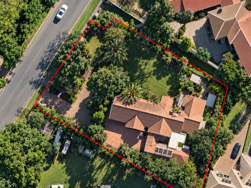 Aerial view of a residential property featuring a large garden, tiled roof, and paved driveway within a suburban neighborhood setting.