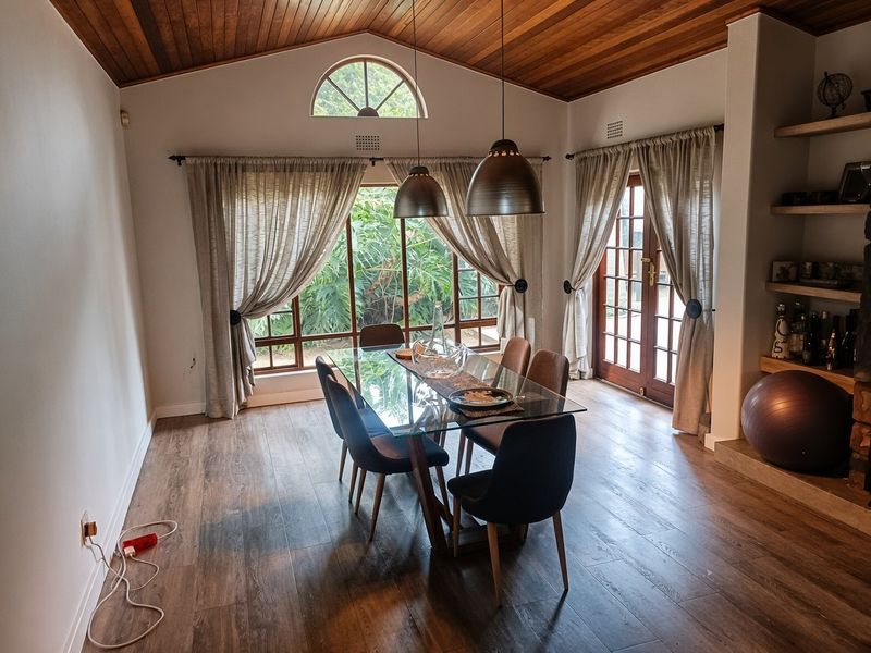Spacious dining room featuring a vaulted timber ceiling, laminate wood flooring, built-in shelving, and direct access to the garden through french doors.
