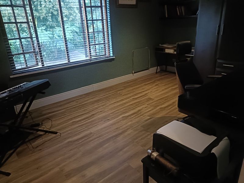 A functional home office space featuring wood-look laminate flooring, built-in shelving, and large windows with venetian blinds providing natural light.