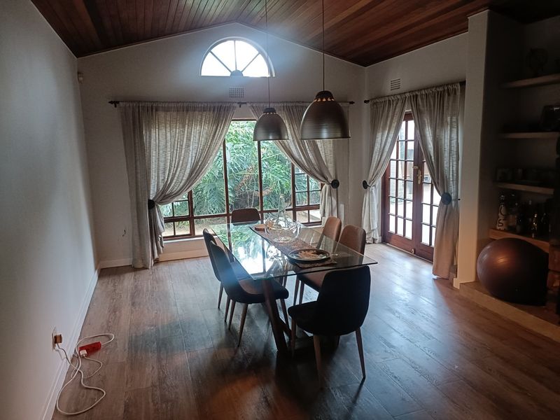 Dining room featuring a timber vaulted ceiling, laminate flooring, pendant lighting, and access to the garden through large windows and french doors.
