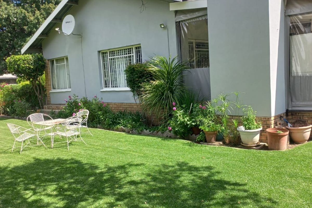 A well-maintained rear garden featuring a lush lawn, a covered patio area, and a prominent chimney stack on the exterior facade.