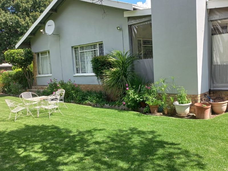 A well-maintained rear garden featuring a lush lawn, a covered patio area, and a prominent chimney stack on the exterior facade.