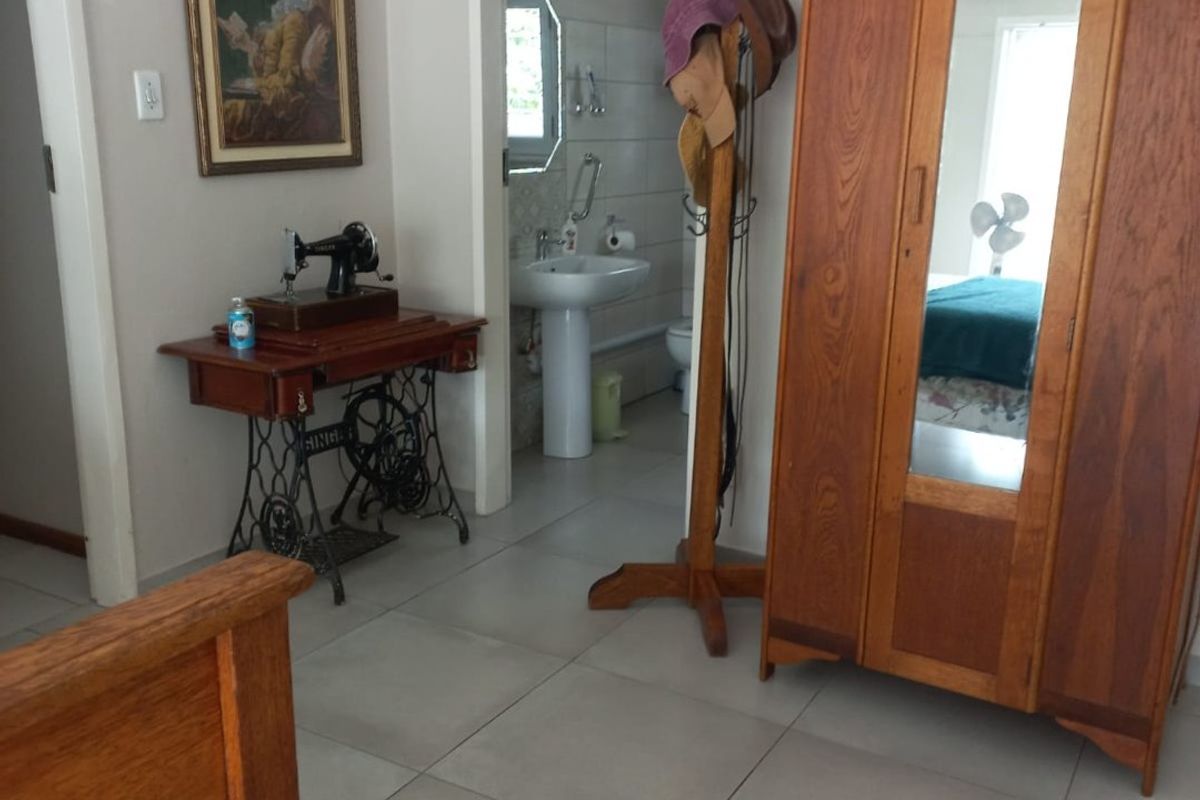 A bedroom featuring neutral tiled flooring with an adjoining bathroom visible, showcasing a pedestal basin and standard interior finishes.