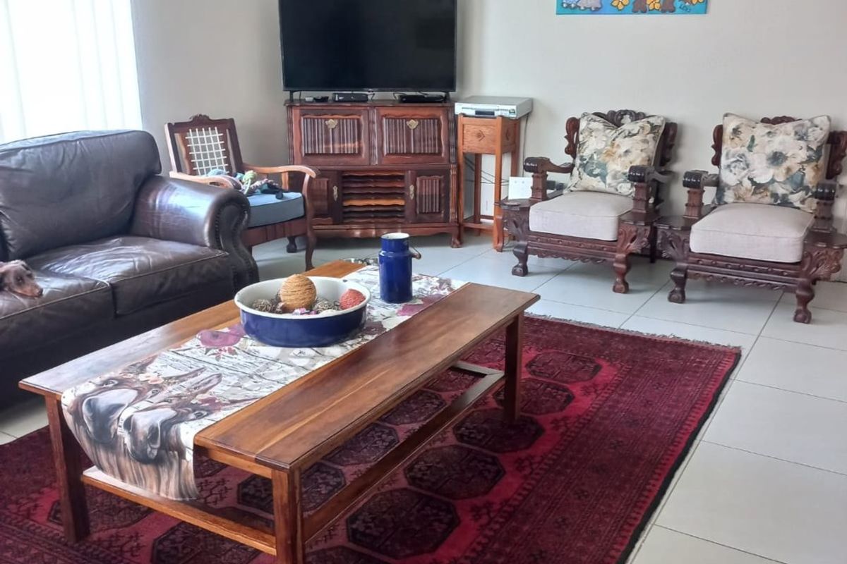 A comfortable living room featuring neutral walls, tiled flooring, and vertical blinds, providing a functional and well-lit space for relaxation.