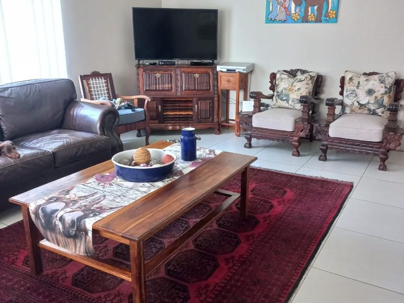 A comfortable living room featuring neutral walls, tiled flooring, and vertical blinds, providing a functional and well-lit space for relaxation.