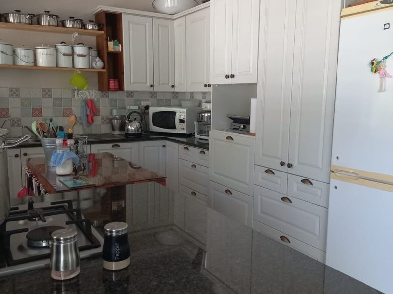 A well-maintained kitchen featuring granite countertops, extensive built-in cabinetry, a gas hob, and a decorative tiled backsplash.