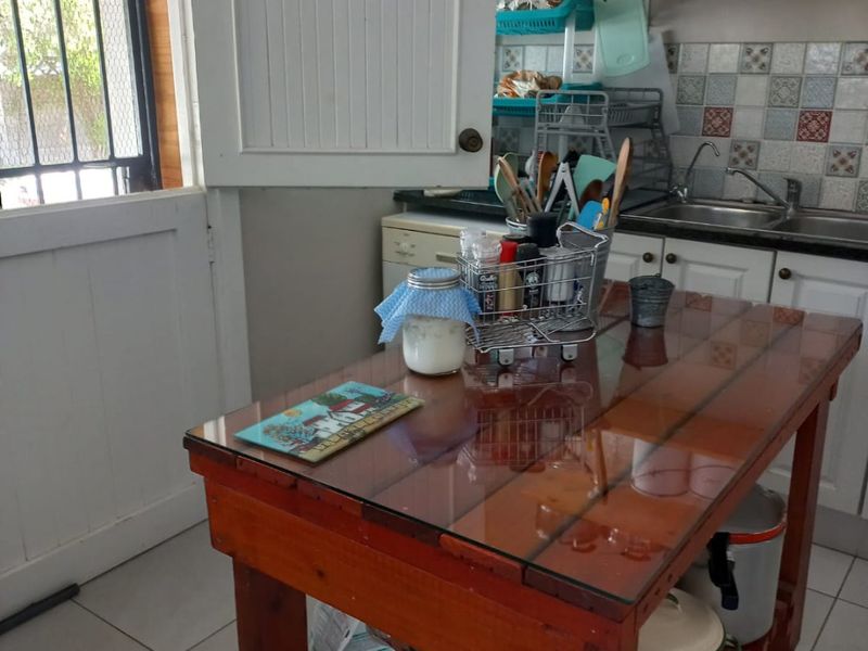 A functional kitchen area featuring tiled flooring, a stainless steel sink, decorative backsplash tiling, and open shelving for storage.