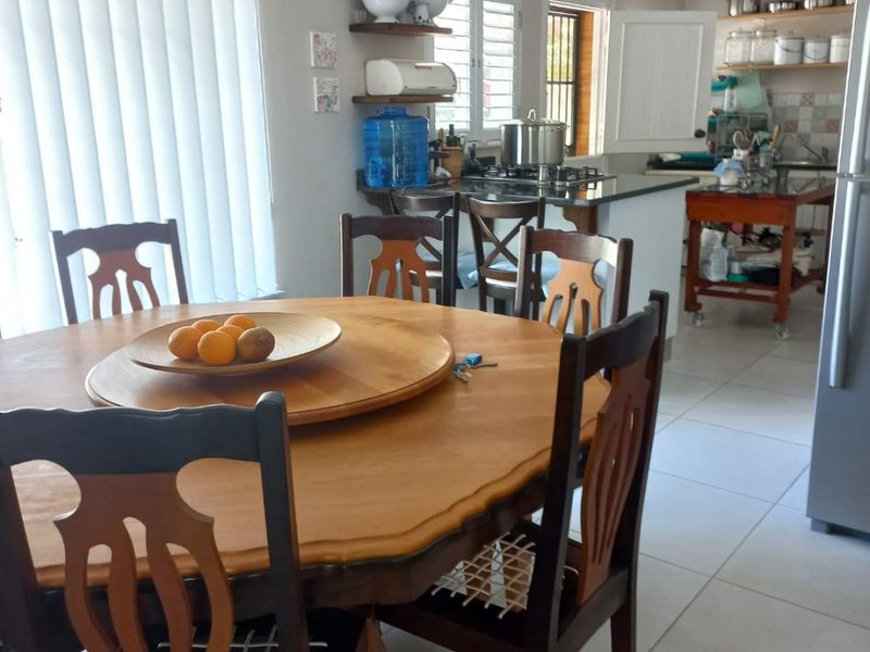 Open-plan kitchen and dining area featuring tiled floors, a central kitchen island with a hob, and ample natural light through vertical blinds.