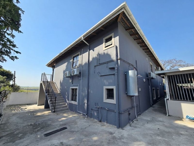 Rear exterior view of the property featuring an external staircase, mounted air conditioning units, and an external geyser on a paved yard.