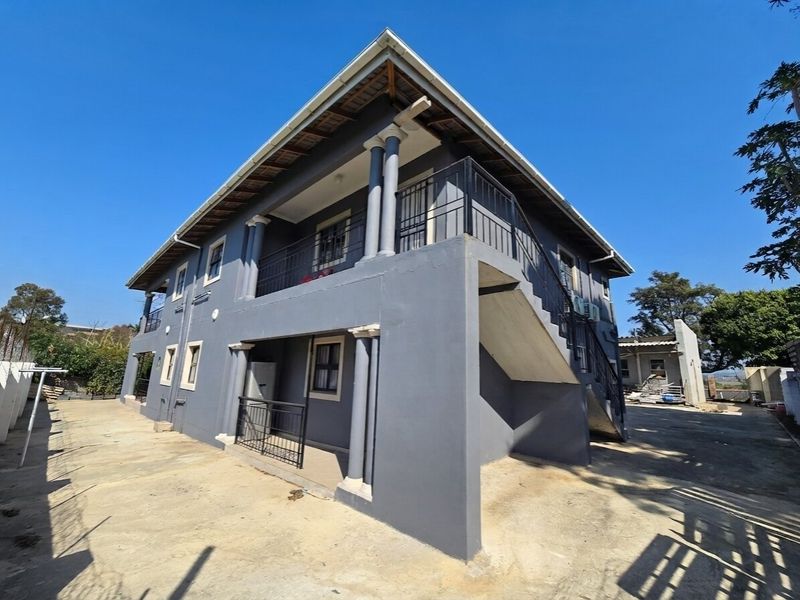 Rear view of a two-story house featuring a concrete staircase, upper balcony with metal railings, and a paved driveway area.