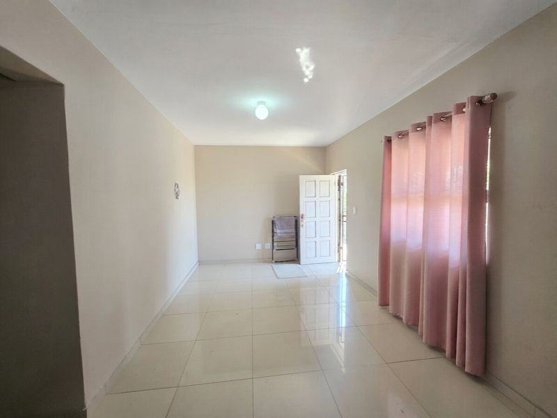 A bright, empty living room featuring neutral wall tones, polished tiled flooring, and a direct entrance door, offering a clean canvas for personalization.