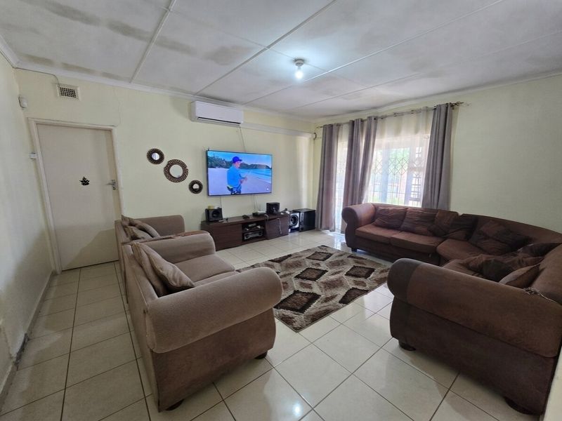 Spacious living room featuring tiled flooring, a wall-mounted air conditioning unit, and access to an outdoor area through a security gate.