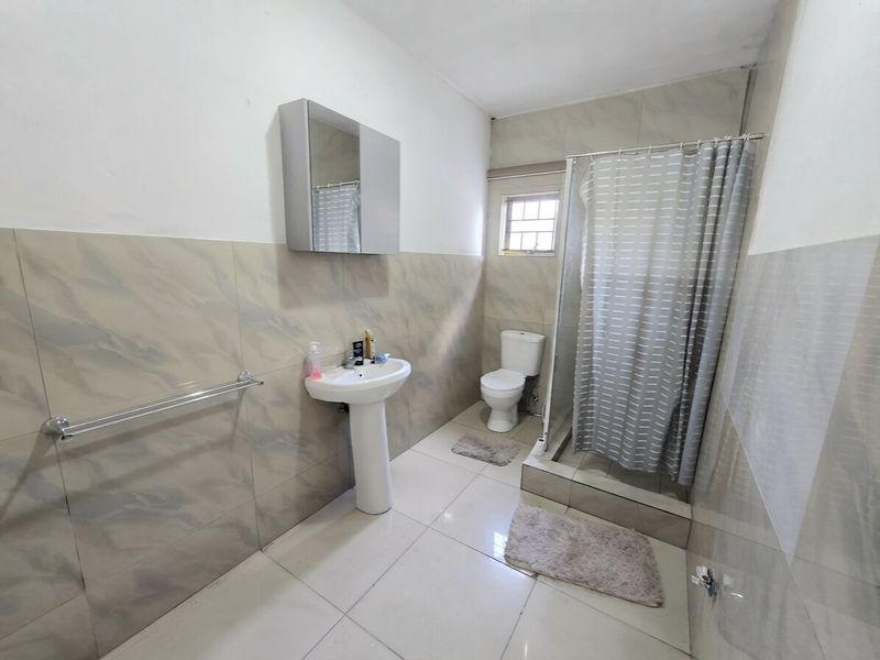 A functional bathroom featuring a pedestal basin, toilet, and a shower enclosure with tiled walls and flooring.