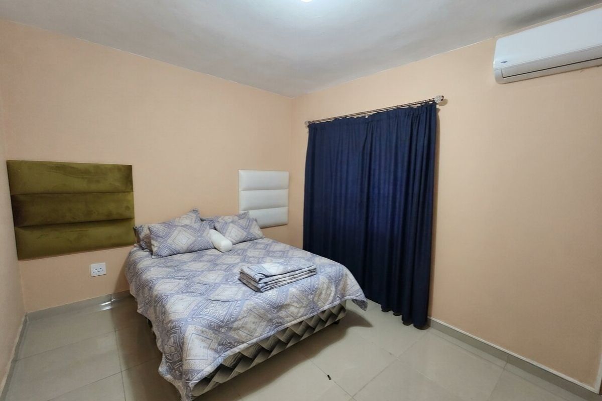A functional bedroom featuring tiled flooring, wall-mounted headboard panels, and a split-system air conditioning unit.