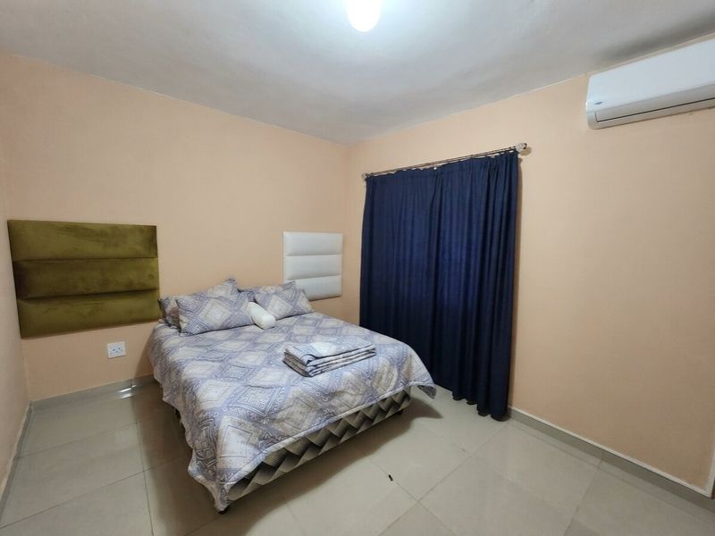 A functional bedroom featuring tiled flooring, wall-mounted headboard panels, and a split-system air conditioning unit.