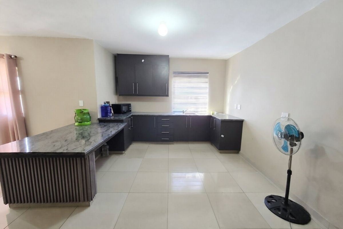A clean, modern kitchen featuring dark cabinetry, stone countertops, a breakfast bar, and neutral tiled flooring, offering a functional and well-maintained workspace.