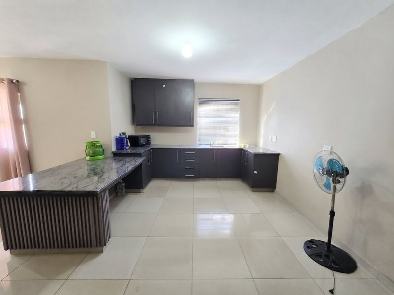 A clean, modern kitchen featuring dark cabinetry, stone countertops, a breakfast bar, and neutral tiled flooring, offering a functional and well-maintained workspace.